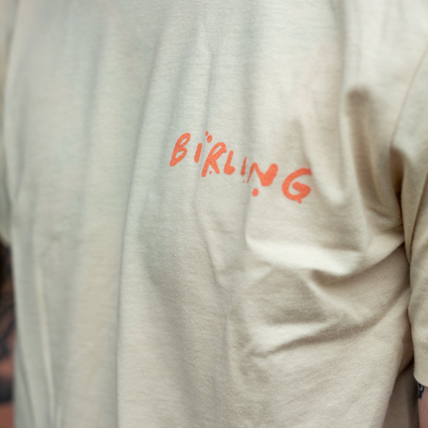 A close-up of a person wearing a cream-colored t-shirt with the word 'BIRLING' printed in orange across the chest.