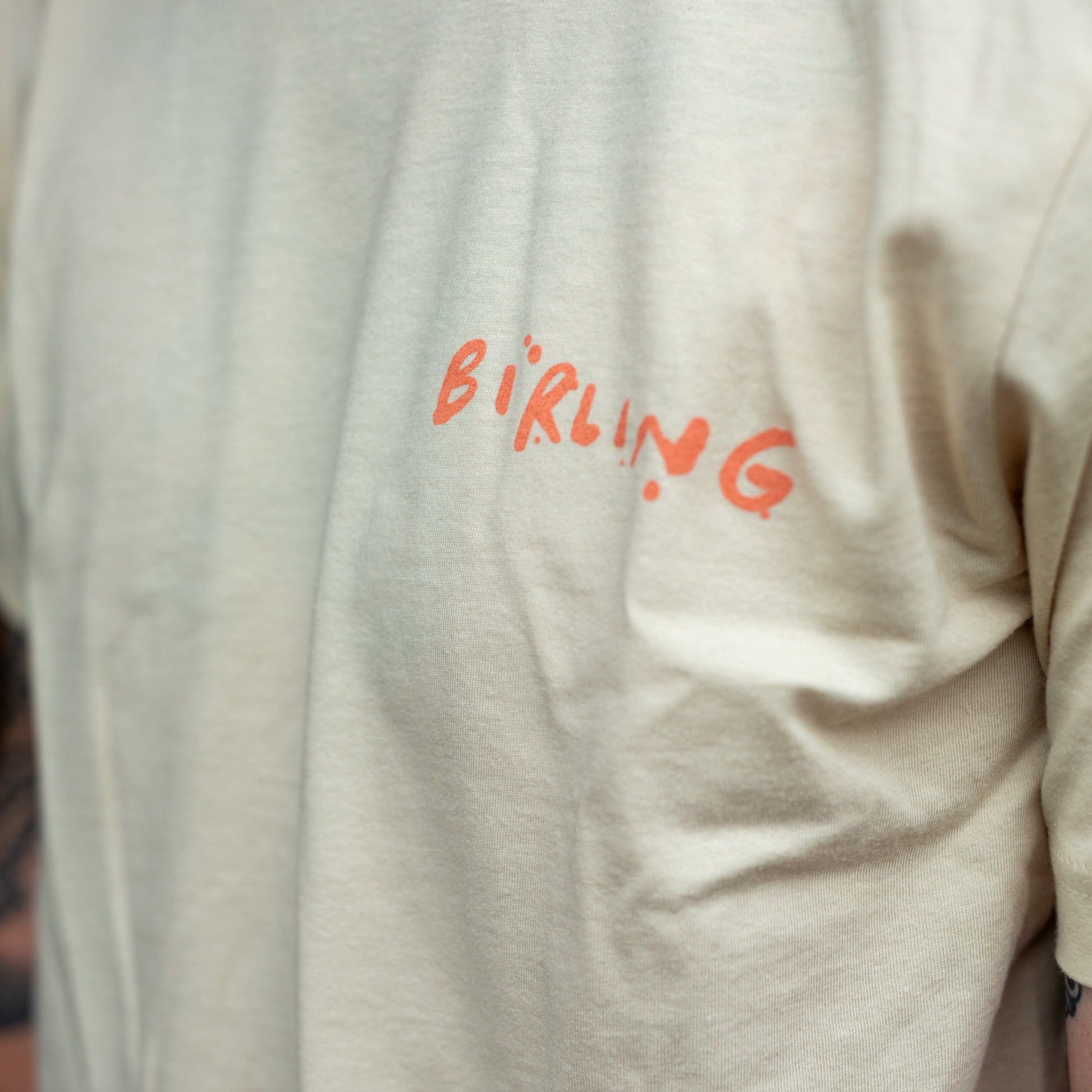 A close-up of a person wearing a cream-colored t-shirt with the word 'BIRLING' printed in orange across the chest.